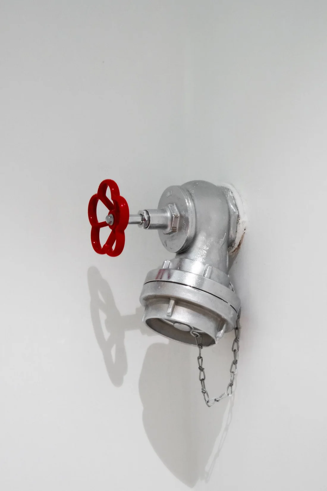 Silver pipe connection and red-handled control valve against a white wall